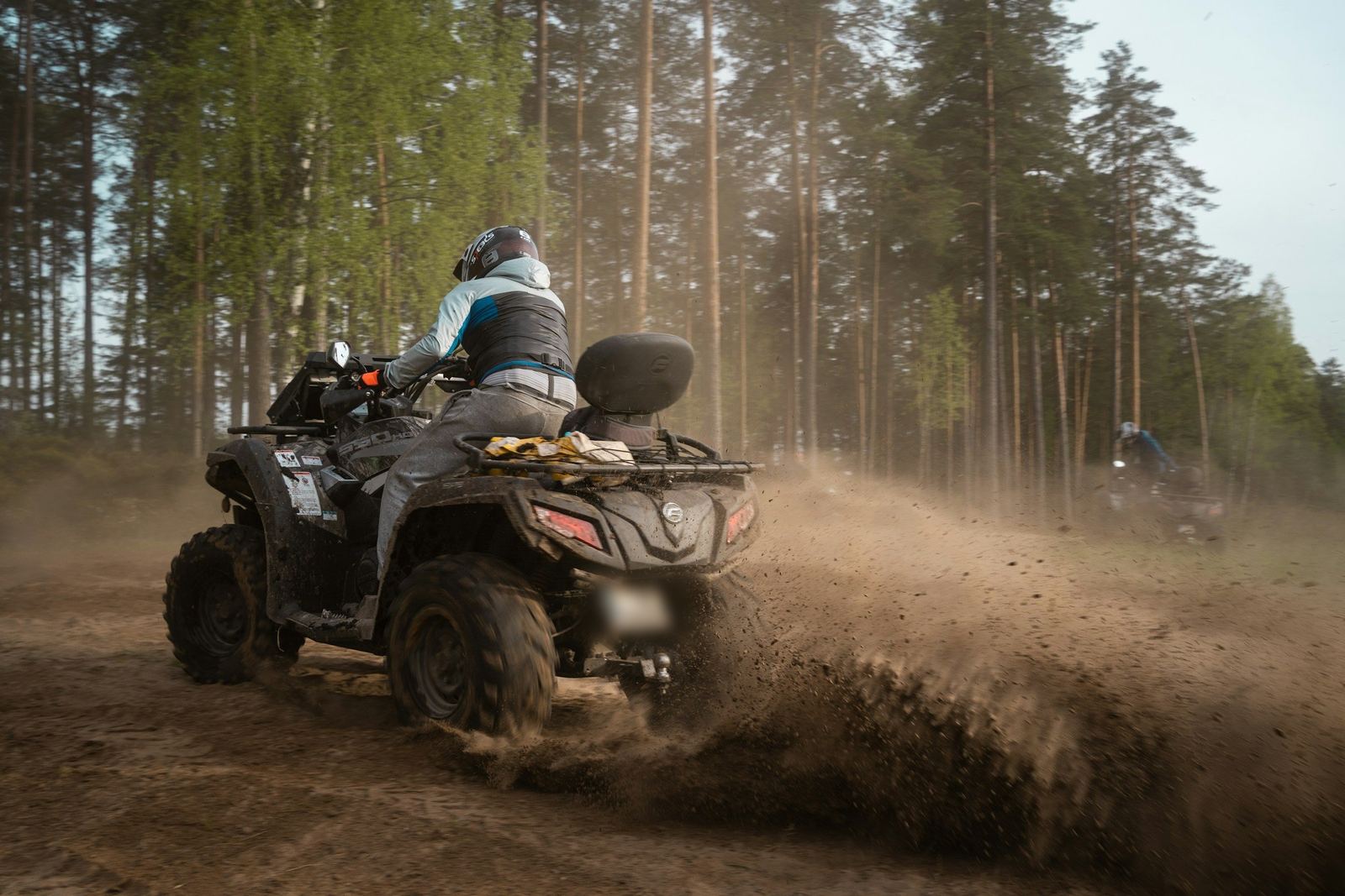 Un quad en travers sur une piste de terre, gerbe de terre projetée, sous une forêt de pins